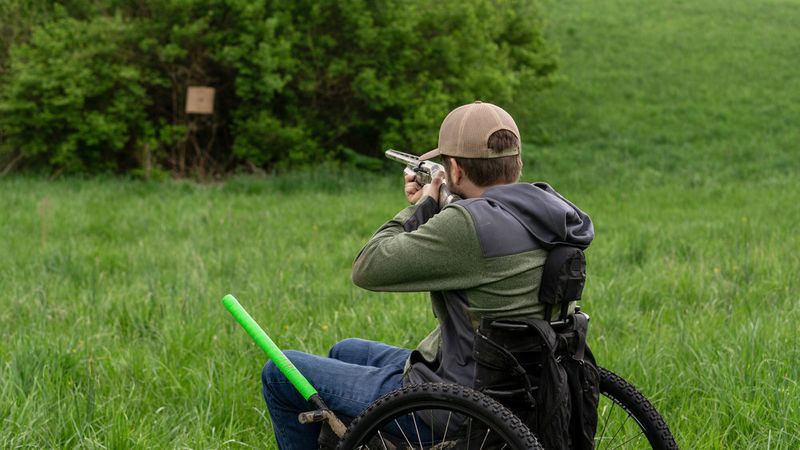 Adaptive Hunting with Ty Hockett: adaptive hunter outside aiming gun while using GRIT Freedom Chair wheelchair outdoors through tall grass