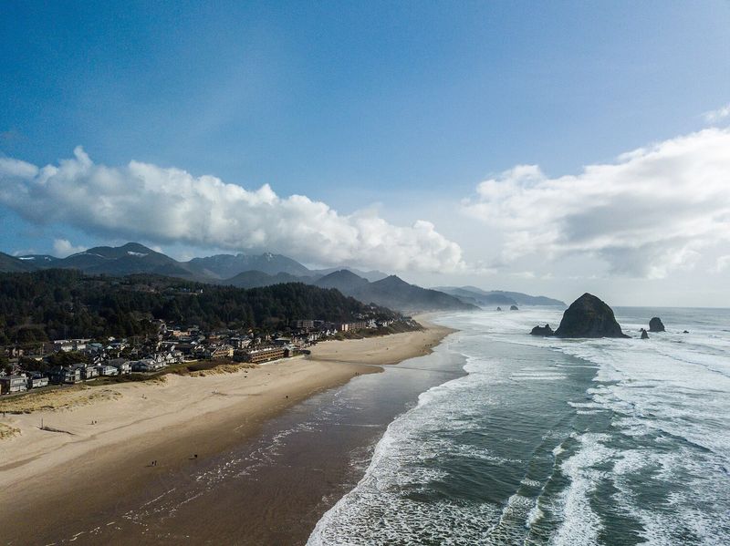 The Best Accessible Beaches on the East and West Coasts, Cannon Beach: mountains and buildings line sandy coast in Clatsop County, Oregon