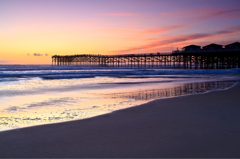 The Best Accessible Beaches on the East and West Coasts, San Diego: tide meets wet sand with pier and multicolored skies at San Diego beach