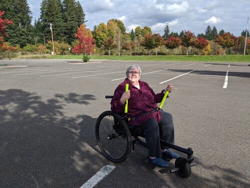 How Easy Is GRIT Freedom Chair To Push or Use for Seniors: Ruth using outdoor GRIT Freedom Chair on paved parking lot near trees and grass