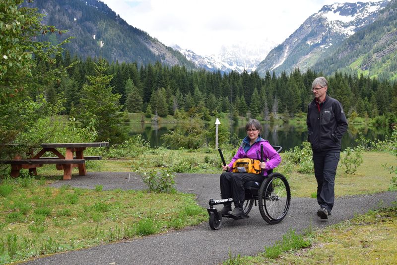 Flying With the GRIT Freedom Chair rider perspective: Jenny Schmitz pushing levers of rugged GRIT wheelchair on gravel path in mountain area