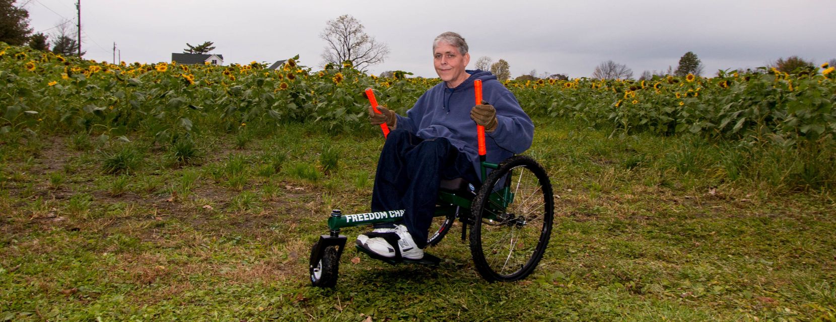 Getting to know my GRIT Freedom Chair: Brad on grass by sunflower field in all-terrain GRIT Freedom Chair wheelchair
