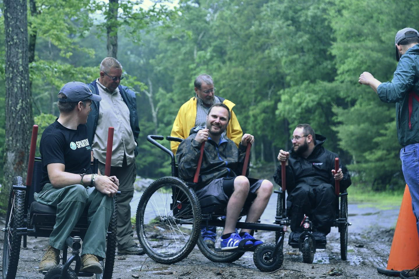 How to choose an all-terrain wheelchair: group of 5 including 3 hikers in GRIT Freedom Chair outdoor wheelchairs, chat on muddy hiking trail