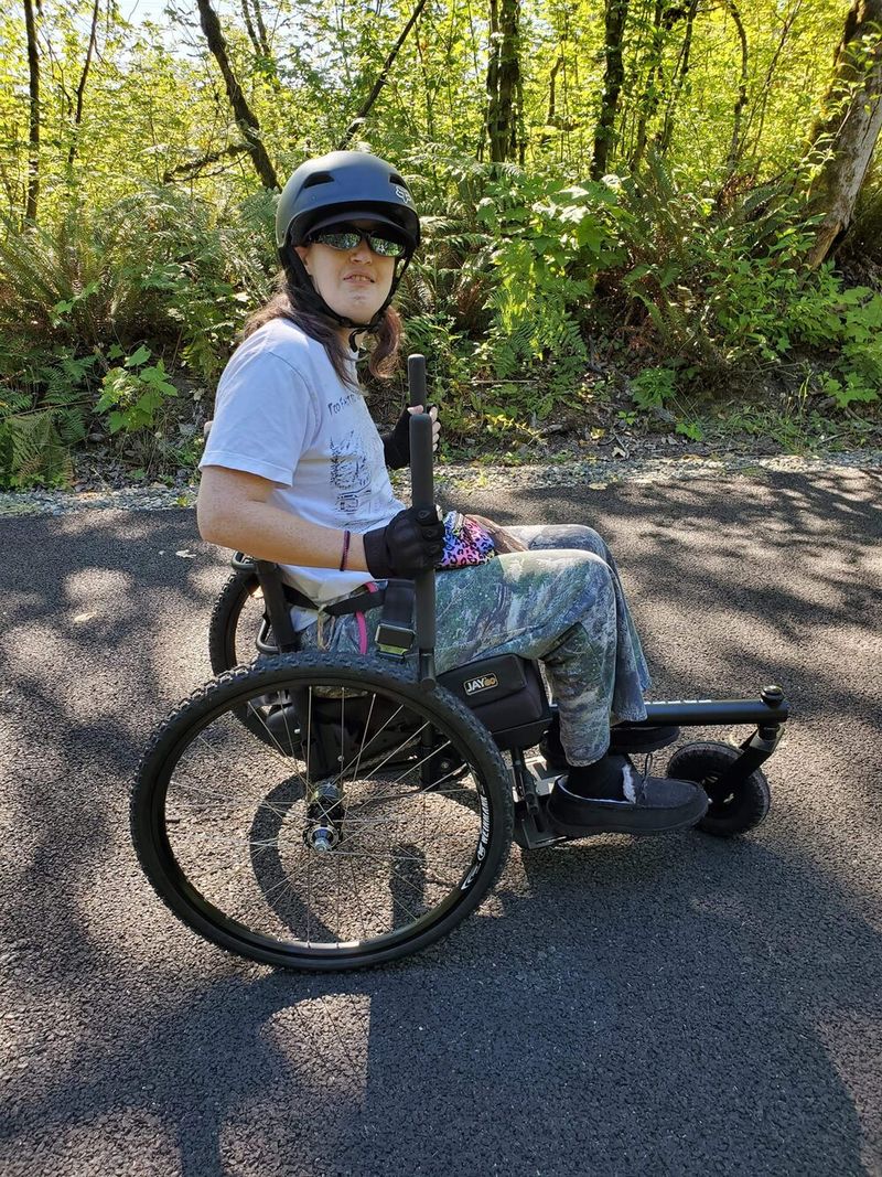 Longevity how to choose all-terrain wheelchair: person riding GRIT Freedom Chair on paved path wearing a helmet