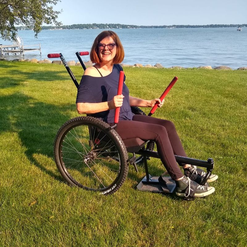 Why Would I Need an Outdoor Wheelchair? Mental and physical health: Robyn smiles riding GRIT Freedom Chair on grass by water at housing area