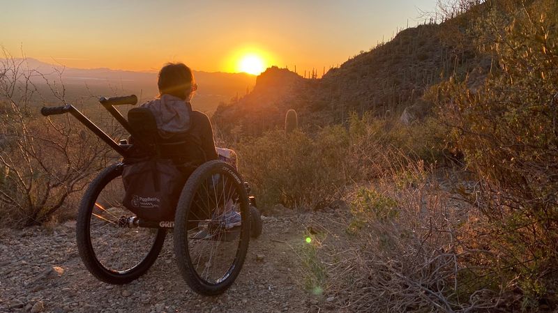 View from behind as Colleen watches sunset over desert hills and plants while using GRIT Freedom Chair outdoor wheelchair