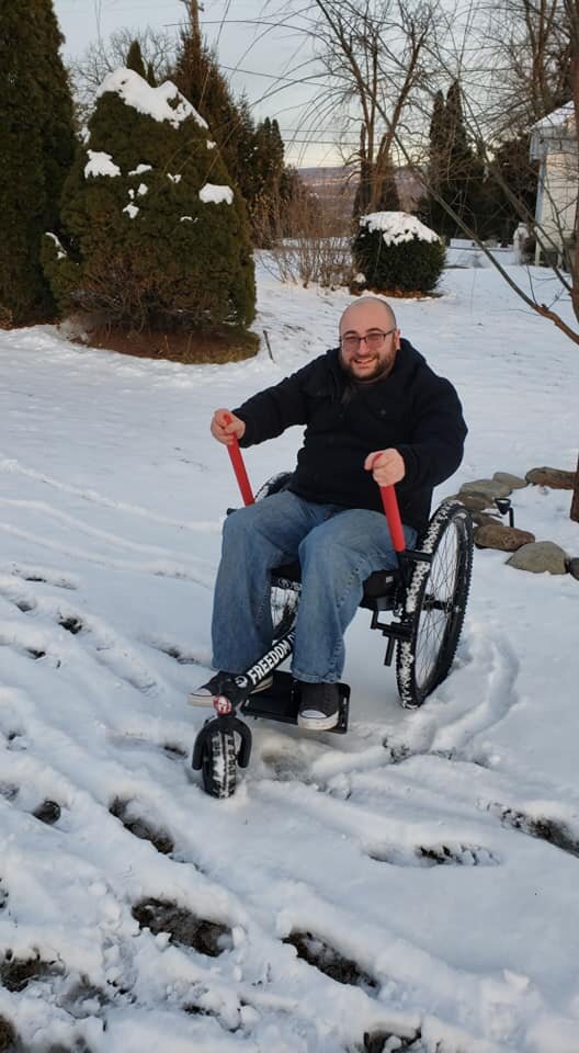 Payment and funding how to choose all-terrain wheelchair: man smiles using GRIT Freedom Chair leaving tracks in the snow