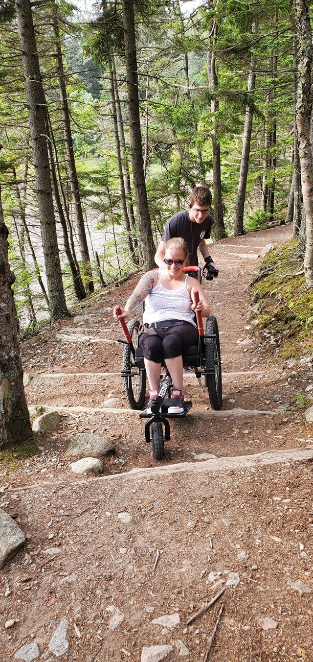Safety how to choose all terrain wheelchair: hiker using GRIT Freedom Chair on bumpy dirt path through woods with trail buddy
